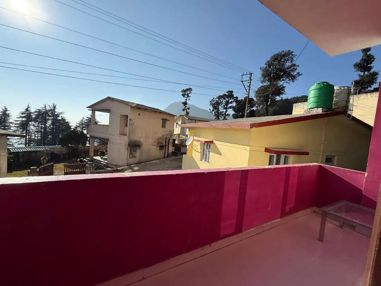 Balcony with a pink parapet looking over nearby buildings, trees and a distant mountain