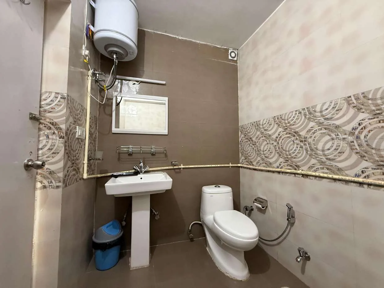 Bathroom with brown and beige tiles, pedestal basin and geyser