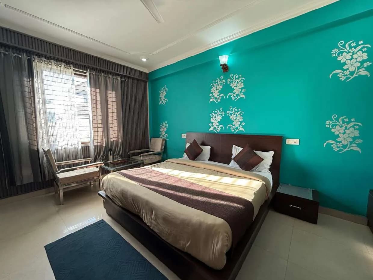 Room with a double bed, green floral wall and a curtained window with armchairs